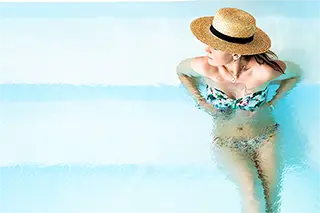 Jeune femme portant un chapeau élégant se prelassant dans une piscine