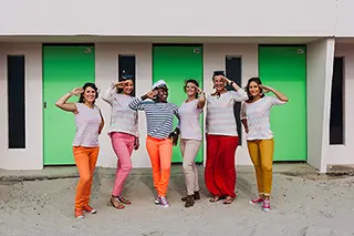 Un groupe de six femmes posant devant des cabines de plage colorées, chacune affichant un style unique avec des pantalons colorés et des expressions joyeuses.