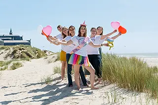 Les femmes, tenant des ballons en forme de cœur, sont alignées le long des dunes de la plage, leur bonheur partagé se reflétant dans la douceur du paysage naturel environnant.