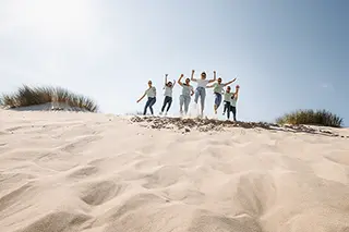 Le groupe d'amies lance un cri de joie au sommet d'une dune, les bras levés vers le ciel bleu, célébrant la vie et leur complicité.
