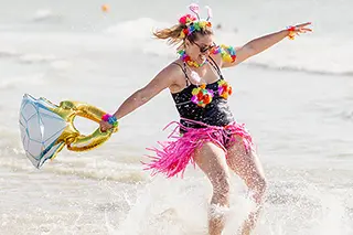 Une femme déguisée danse au rythme des vagues, éclaboussant l'eau autour d'elle dans un mouvement plein de vie et de gaieté.
