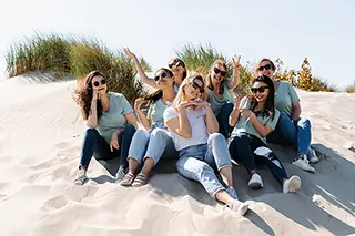 Un groupe de jeunes femmes pose de manière détendue sur les dunes de sable, leurs lunettes de soleil et sourires reflétant l'insouciance d'un après-midi ensoleillé.