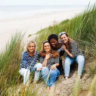 Assises tranquillement dans les dunes, quatre amies partagent des sourires et des moments de complicité, profitant de la sérénité du paysage naturel environnant.