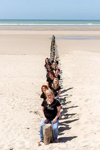 Des amies posent en file indienne le long d'un brise-lames, créant une perspective captivante avec le sable et la mer en toile de fond.
