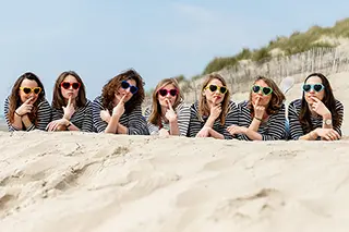 Allongées sur le sable, ces amies aux lunettes de soleil coordonnées partagent un moment de complicité, comme si elles partageaient des secrets en un chuchotement collectif.