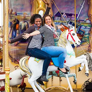 Deux amies partagent des rires contagieux sur un carrousel coloré, leur joie et leur insouciance capturées dans un moment de plaisir enfantin.