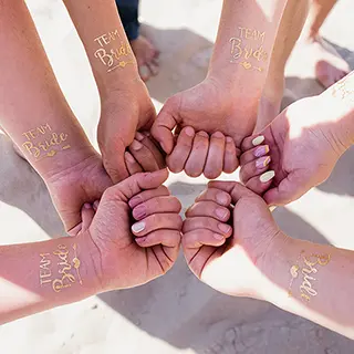Un cercle d'amitié est formé par des mains jointes, tatouées de mots de célébration, symbolisant l'union et la joie d'un moment de vie partagé.