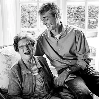 Une dame âgée et un homme riant ensemble dans une pièce lumineuse