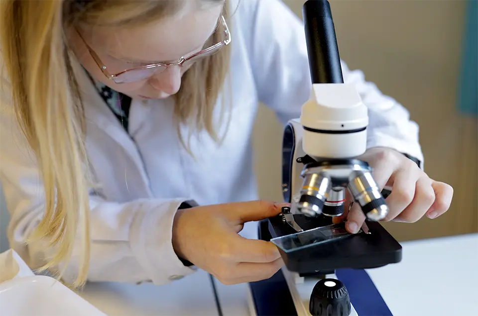 Jeune étudiante utilisant un microscope dans un laboratoire de sciences