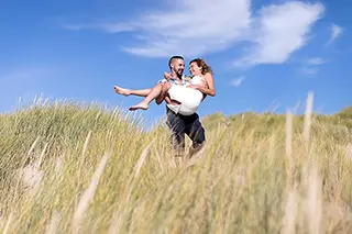 Homme portant sa partenaire enceinte sur une dune sous un ciel bleu