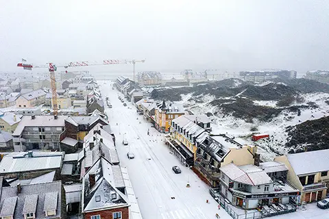 Galop sur la plage Vue aérienne d'une ville enneigée avec des toits blancs, des rues couvertes de neige et des dunes en arrière-plan sous un ciel brumeux