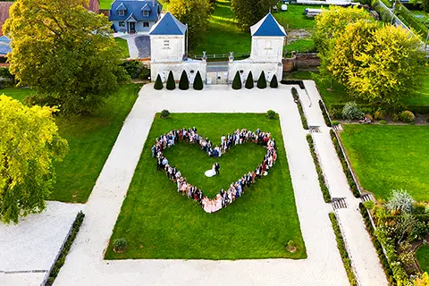 Galop sur la plage Vue aérienne d'un rassemblement formant un cœur sur la pelouse verte des jardins d'un château, entourée d'allées et de bâtiments élégants, lors d'un événement festif