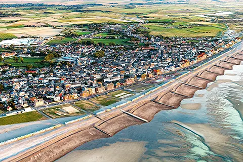 Galop sur la plage Vue aérienne d'une ville côtière avec des plages, des cabines de bain alignées, et des champs verdoyants en arrière-plan
