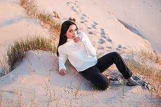 Femme pensante assise sur une dune de sable au crépuscule.